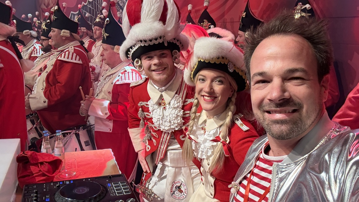 DJ René Braun am Pult mit dem aktuellen Tanzpaar der Roten Funken, im Hintergrund das Korps